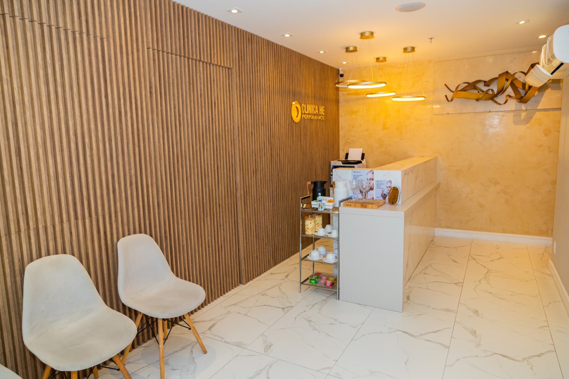 Sala de espera com poltronas claras e pendentes dourados